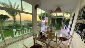 A dining area with a table and chairs, large windows with a view of greenery and a fence, and a ceiling fan.