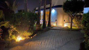 A pathway leading to a building with a curved facade, palm trees, and a lit lantern.