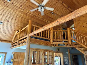 L’intérieur d’un chalet en bois, doté d’un balcon, de meubles en bois et d’un ventilateur de plafond.