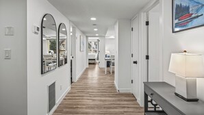 Un couloir avec un plancher en bois, des murs blancs et une lampe posée sur une table.