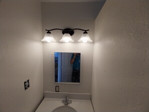 Un baño con lavamanos blanco, un espejo y tres luces fijadas a la pared.