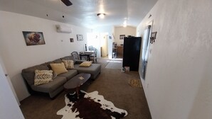 Ein Wohnzimmer mit Ecksofa, Couchtisch, Kuhfellteppich und Deckenventilator.
