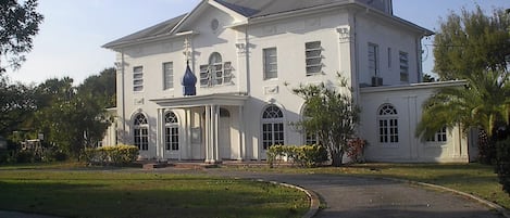 A large, white, two-story building with a symmetrical facade, a central entrance with columns, and a blue dome-like structure above it.