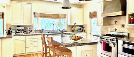A spacious kitchen with wooden cabinets, a central island with bar stools, a gas stove, and a large window providing natural light.