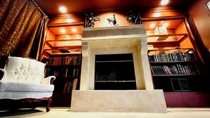 Une bibliothèque dotée d’une cheminée, d’étagères et d’un fauteuil moelleux.