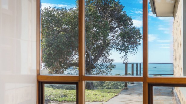 Une salle de bain dotée d’une grande fenêtre donnant sur un sentier de pierre menant à la plage.