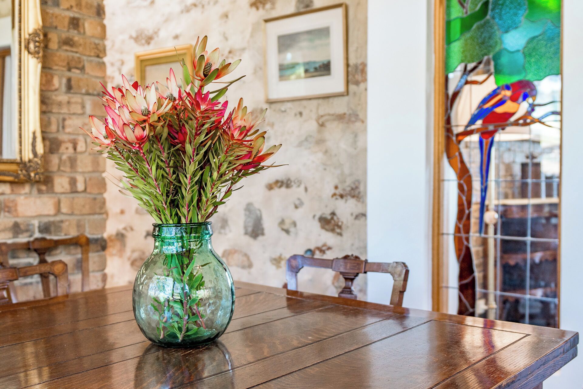 A green glass vase with red and green foliage on a wooden table.
