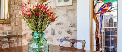 A green glass vase with red and green foliage on a wooden table.