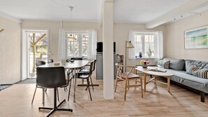 Amplia sala de estar con una mesa de comedor, sillas, un sofá y una mesa de centro. Grandes ventanales ofrecen luz natural y vistas al exterior.