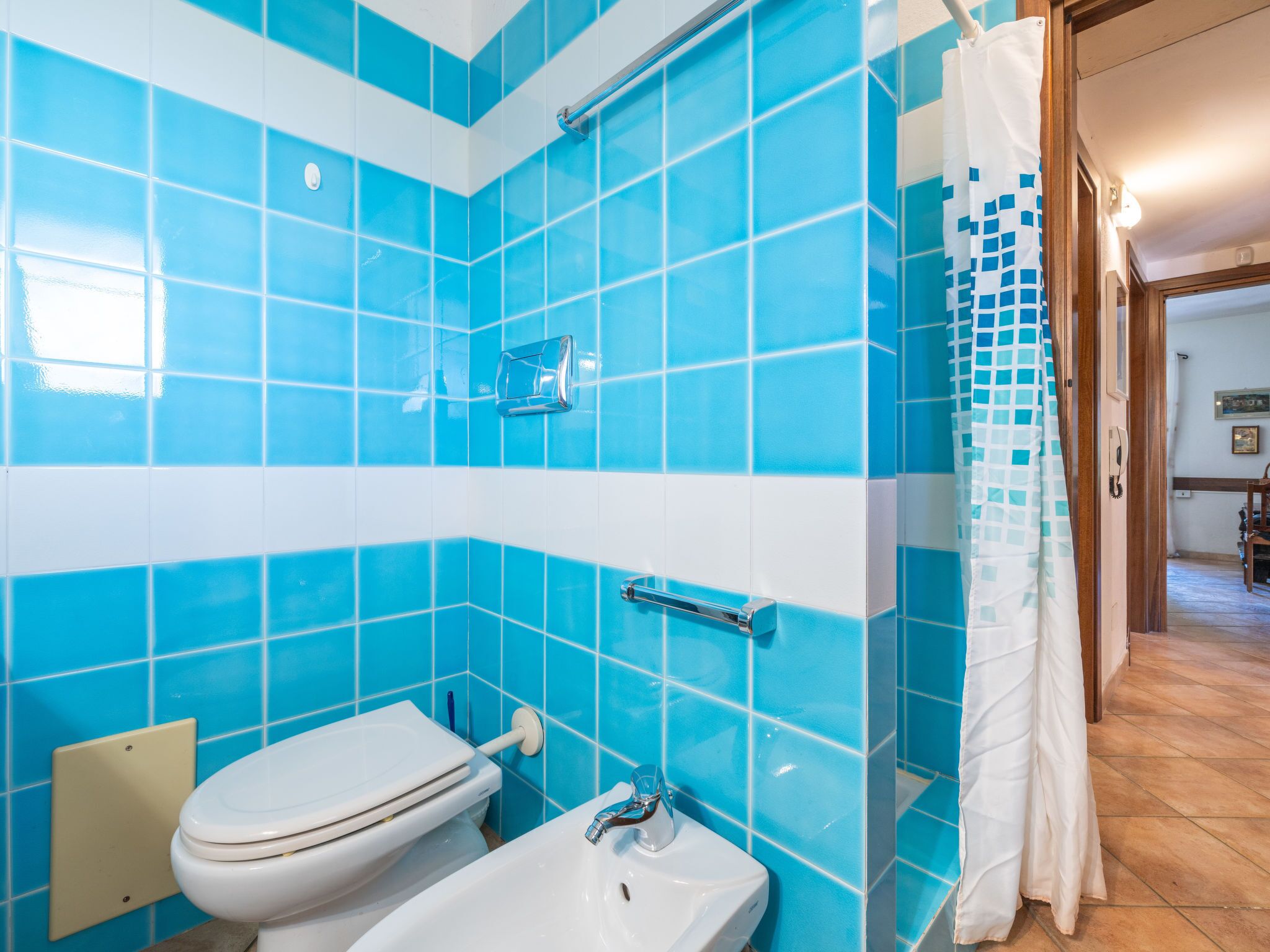Ein Badezimmer mit blauen Fliesen, einer weißen Toilette, einem weißen Waschbecken und einer Duschvorhang.