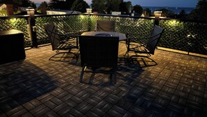 Une terrasse extérieure avec une table ronde et quatre chaises, entourée d’un sol en briques et d’une rambarde en métal.