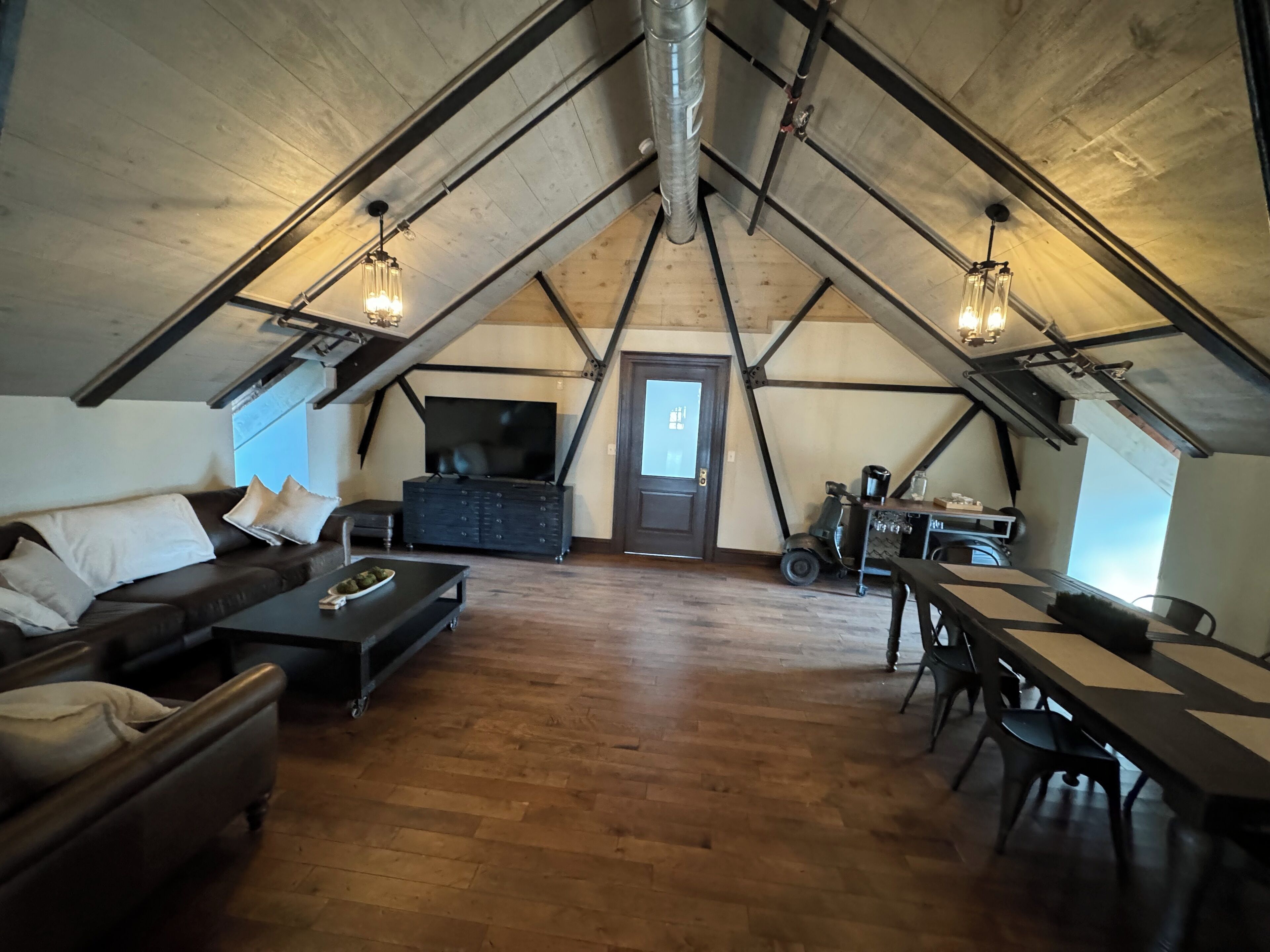 A loft-style room with a wooden floor, a sofa, a coffee table, a TV, and a dining area with chairs and a table.