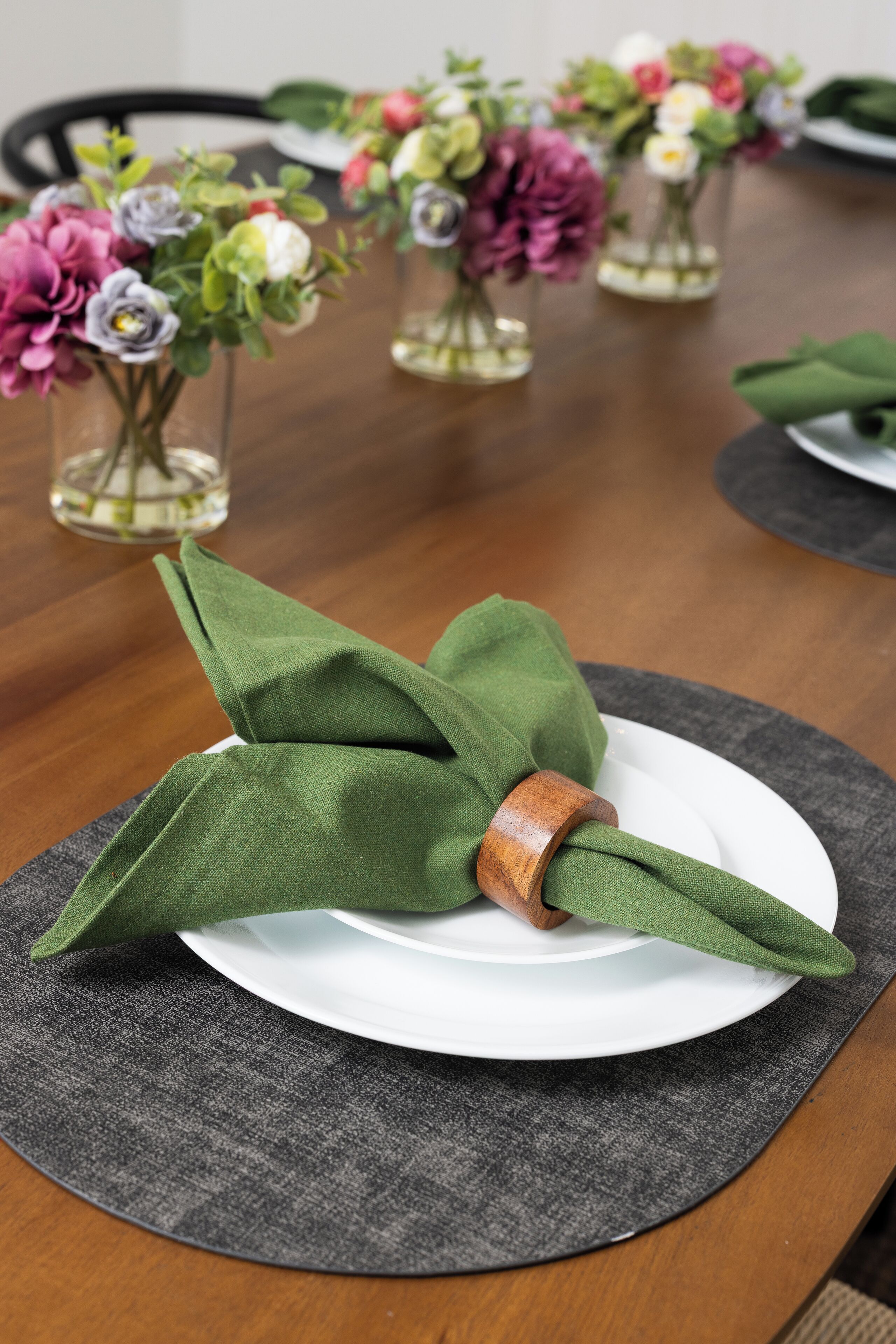 Una mesa con un anillo de servilleta verde sobre un plato blanco, rodeada de pequeños floreros con flores.