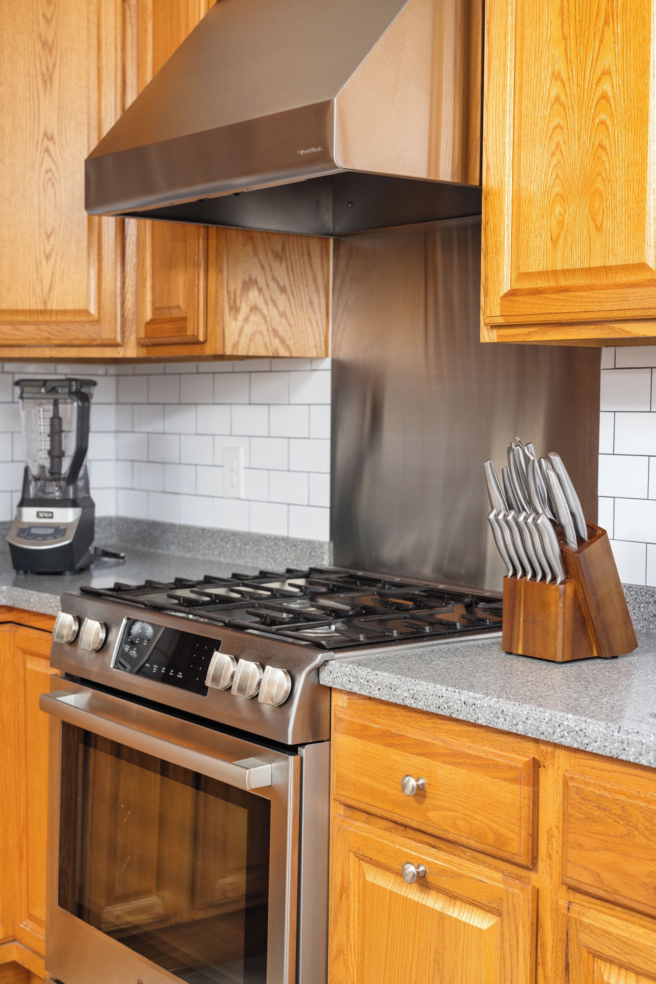 A kitchen with wooden cabinets, a stainless steel range hood, a gas stove, an oven, and a knife block on the countertop.