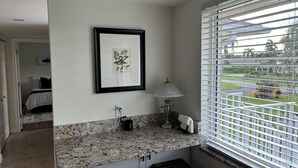 A bathroom with a granite countertop, a framed picture, a lamp, and a window with blinds. - Resort - Style Condo in Naples, Florida (Naples)
