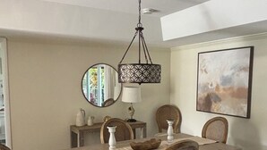 A dining area with a wooden table, six chairs, a hanging light fixture, a mirror, and a painting on the wall. - Resort - Style Condo in Naples, Florida (Naples)