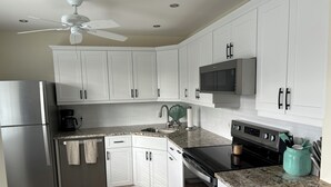 A modern kitchen with white cabinets, a stainless steel refrigerator, a microwave, an oven, and granite countertops. - Resort - Style Condo in Naples, Florida (Naples)