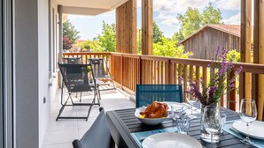 A balcony with a dining table set for two, a chair, and a wooden railing. - Jade et Elena by Interhome (Lit-et-Mixe)