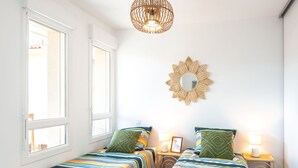 A room with two beds, each with striped bedding, a round mirror on the wall, and a hanging light fixture. - Jade et Elena by Interhome (Lit-et-Mixe)