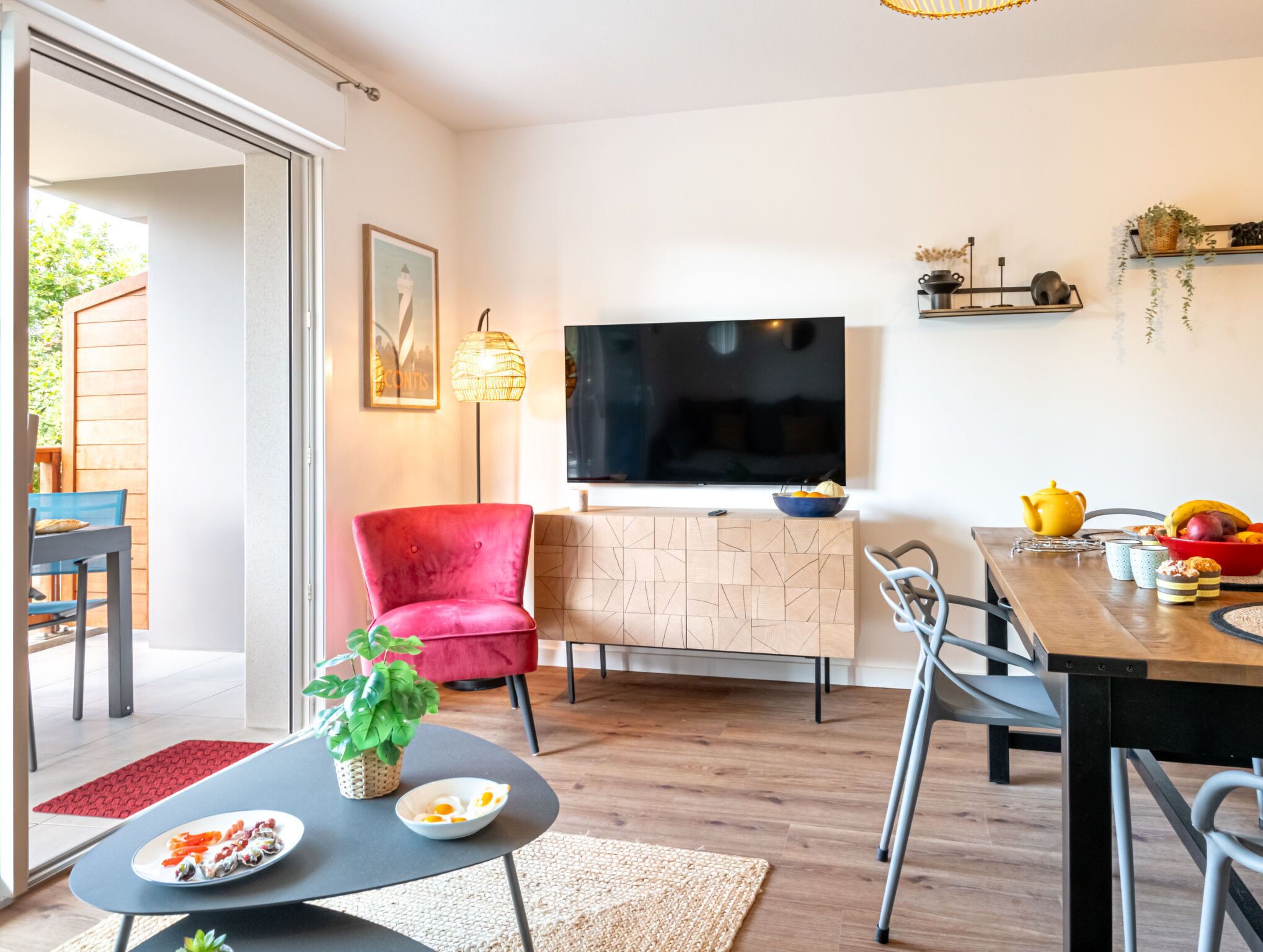 A modern living room with a red chair, a TV, and a dining area with a table set for two.