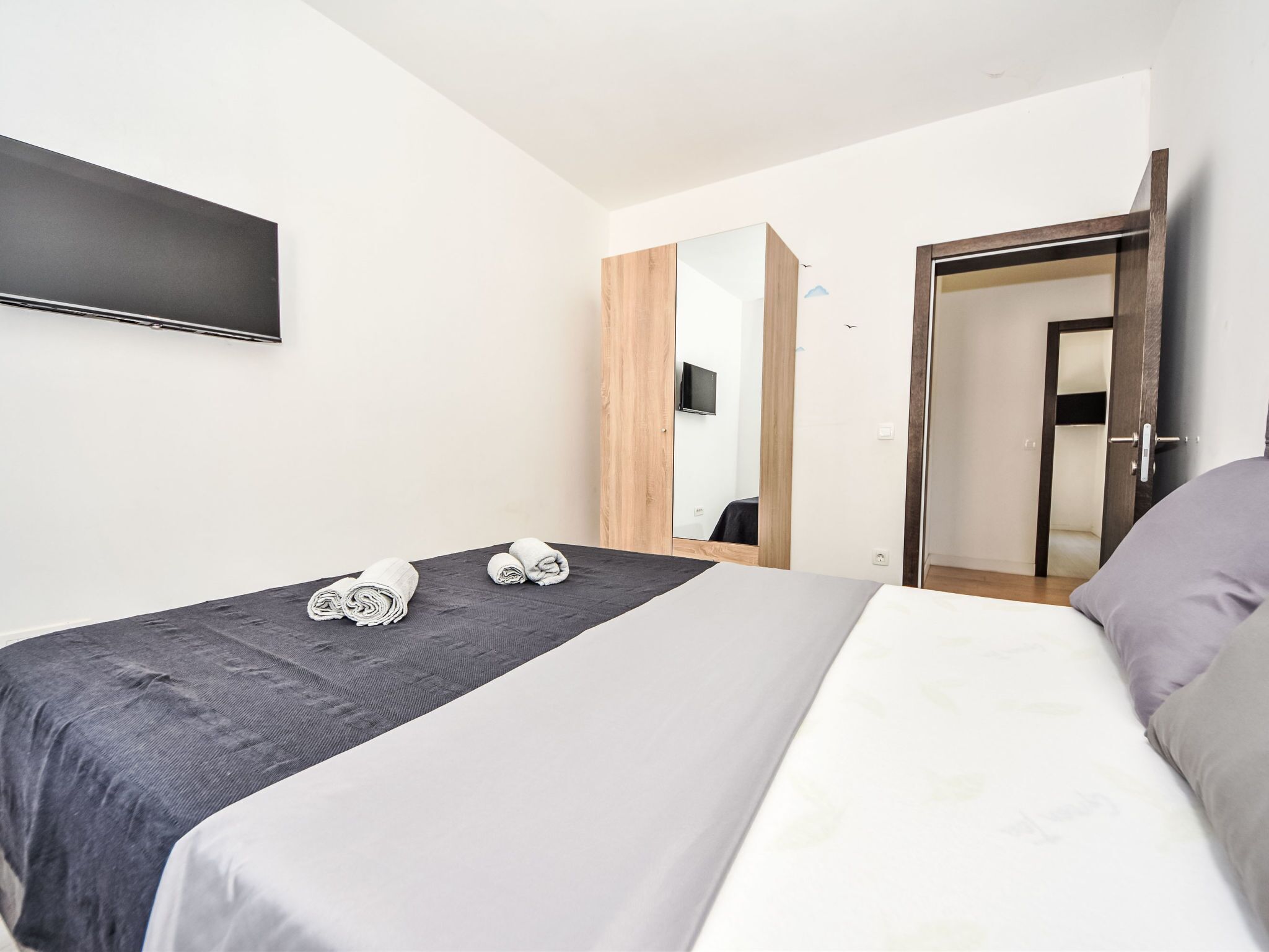 A modern bedroom with a bed, a TV mounted on the wall, and a wooden wardrobe.
