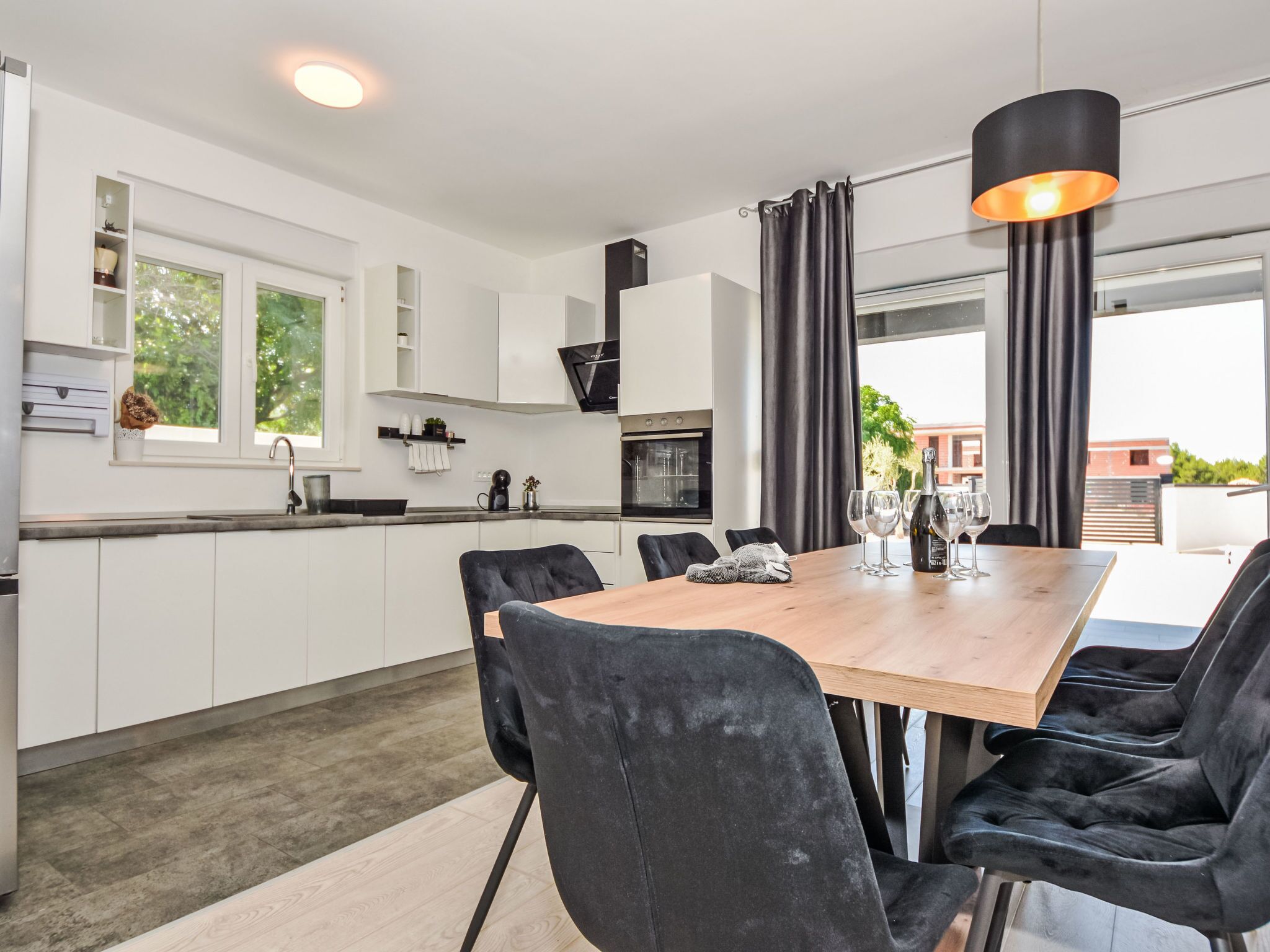 Une cuisine moderne avec des meubles blancs, une table à manger en bois et des chaises noires.
