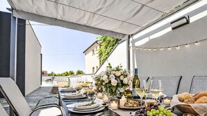 An outdoor dining setup with a table set for a meal, including plates, glasses, and candles.