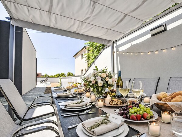 Un espace de restauration en plein air avec une table dressée pour un repas, comprenant des assiettes, des verres et des bougies.