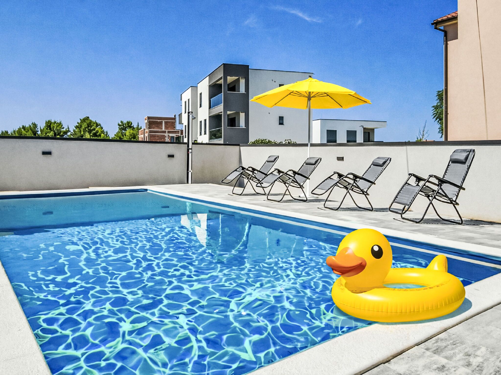 A swimming pool with clear blue water, surrounded by lounge chairs and a yellow umbrella.