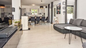 A modern living room with a grey sofa, a small white table, and a dining area with a kitchen in the background.