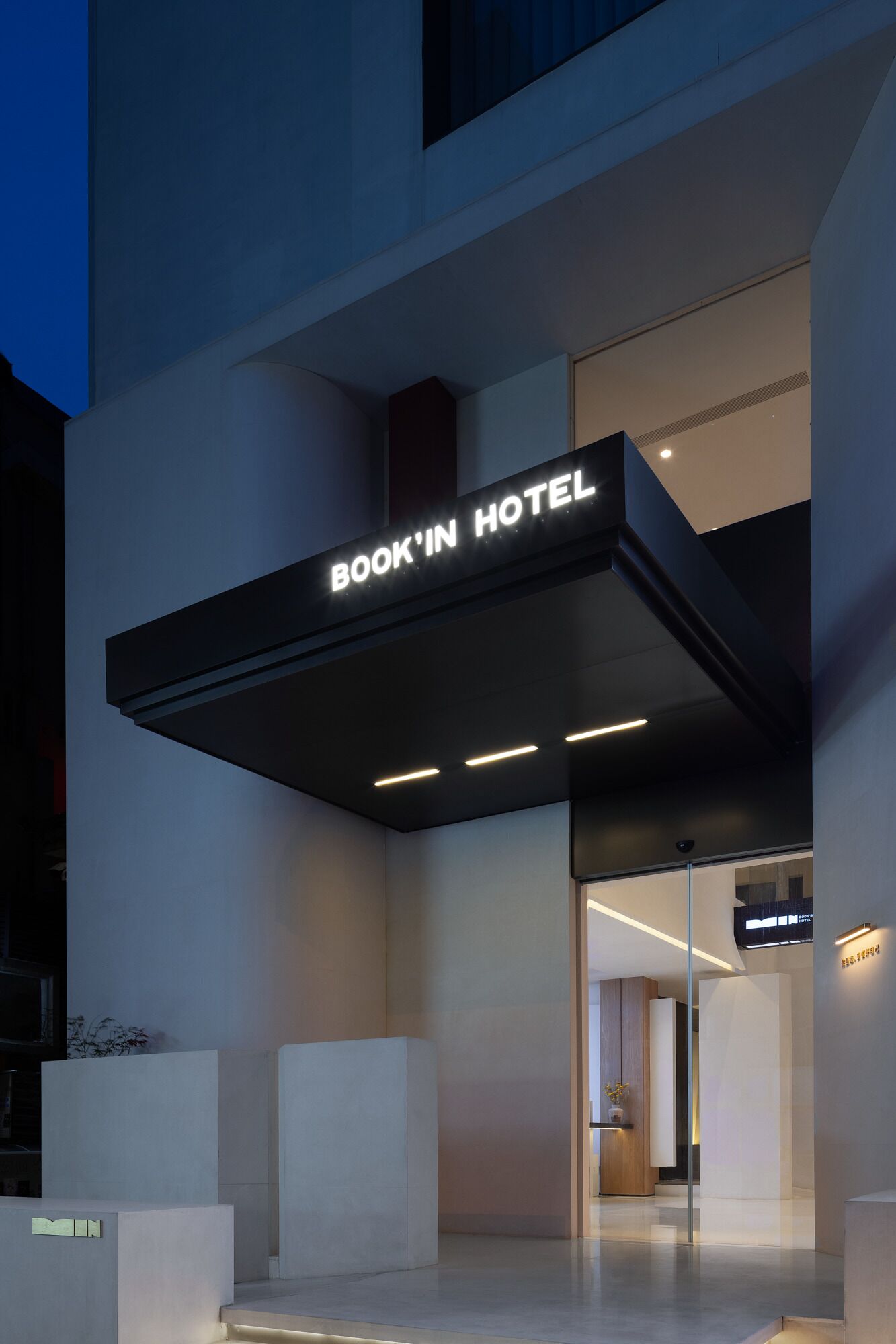 Una entrada de hotel moderna con un letrero que dice 'BOOK IN HOTEL', una puerta de cristal y un diseño limpio y minimalista.