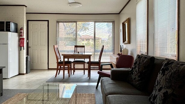 A spacious living room with a glass coffee table, a sofa, and a dining area with chairs. - Little Gem in the City (Braddon)