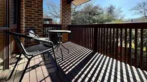 A wooden deck with a table and chairs, a brick wall, and a view of trees and a house. - Little Gem in the City (Braddon)