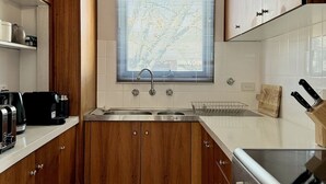 A modern kitchen with wooden cabinets, a stainless steel sink, and a built-in oven. - Little Gem in the City (Braddon)