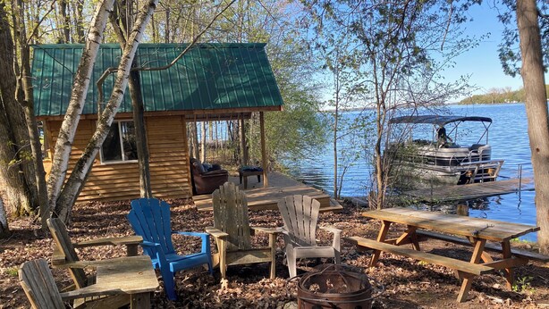 Eine Hütte mit einer Terrasse mit Blick auf einen See, ausgestattet mit Sitzgelegenheiten im Freien und einer Feuerstelle.