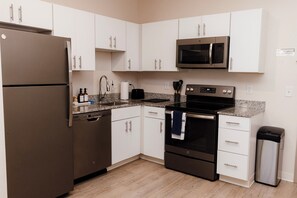 Una cucina moderna con mobili bianchi, un frigorifero in acciaio inox, un forno a microonde, un forno e un lavello.