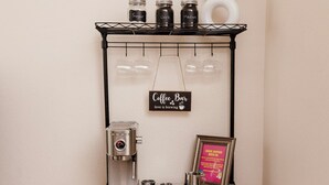 Een koffiebar inrichting met een koffiemachine, suiker- en roomhouders op een zwart metalen rek, een bord met de tekst 