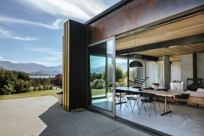 A modern house with a large glass door leading to an outdoor dining area with a table and chairs. - Te Pakeke - Couples Retreat - Lake Views (Wanaka)
