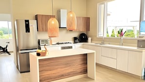 A modern kitchen with a central island, stainless steel appliances, wooden cabinets, pendant lighting, and a view of greenery outside. - Mágica CASA FINCA de lujo piscina wi-fi (San Sebastian de Mariquita)