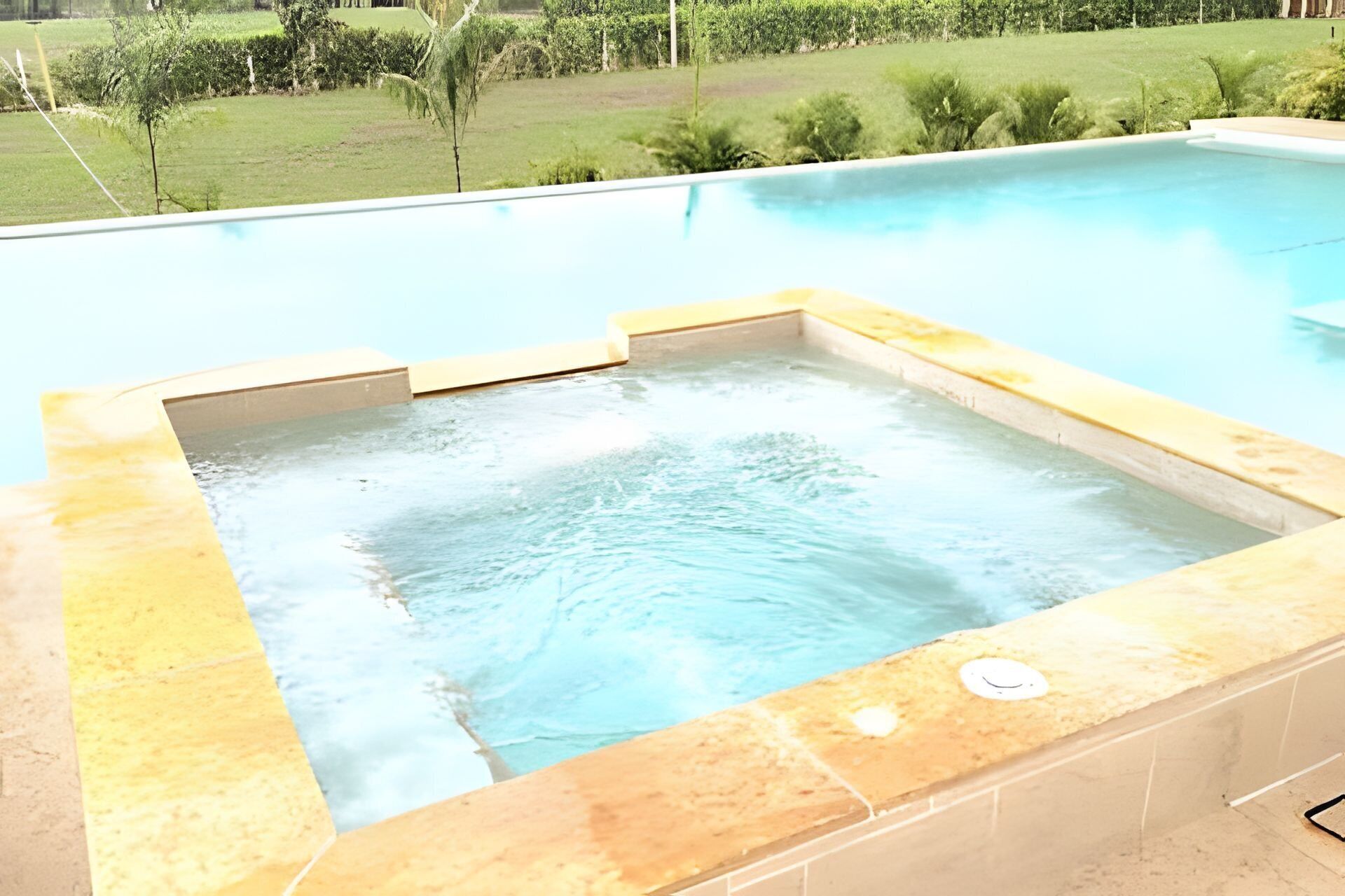 A swimming pool with a hot tub in the center, surrounded by a tiled deck.