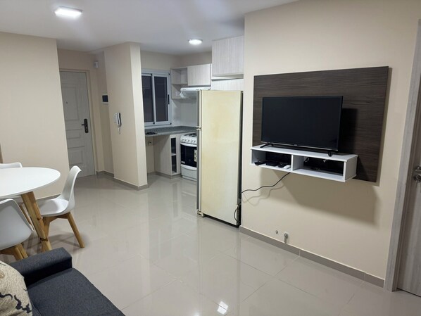 A modern kitchen with white cabinets, a built-in oven, and a refrigerator. There is a dining area with a white table and chairs.