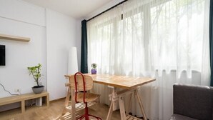 A room with a wooden desk, a chair, a bench, a sofa, and a window with sheer curtains. - Jazzy Studio in the Heart of Bucharest (București)