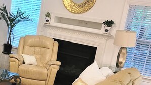 A living room with a fireplace, a ceiling fan, a large mirror, and a potted plant.