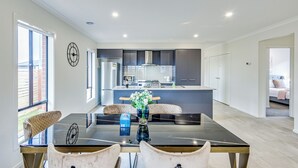 A modern kitchen with a central island, a dining area with a glass table, and a living space with a bed and a view of the outdoors.