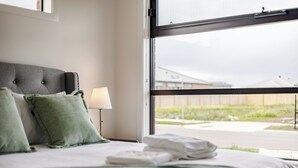 A hotel room with a bed, green pillows, a lamp, and a view of the outside.