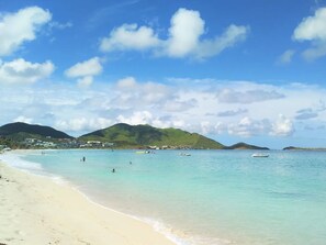 A beach with clear turquoise water, a sandy shore, and a backdrop of green hills. - Logement 40 m2, front de mer à 50 m de la plage (Cul-de-Sac)