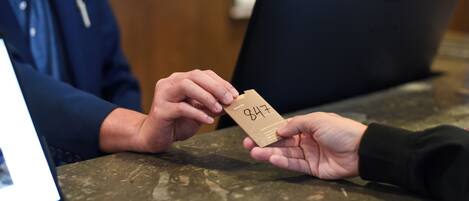 Une personne tient une carte portant le numéro 847 devant un comptoir où se trouvent un ordinateur portable et une chaise.