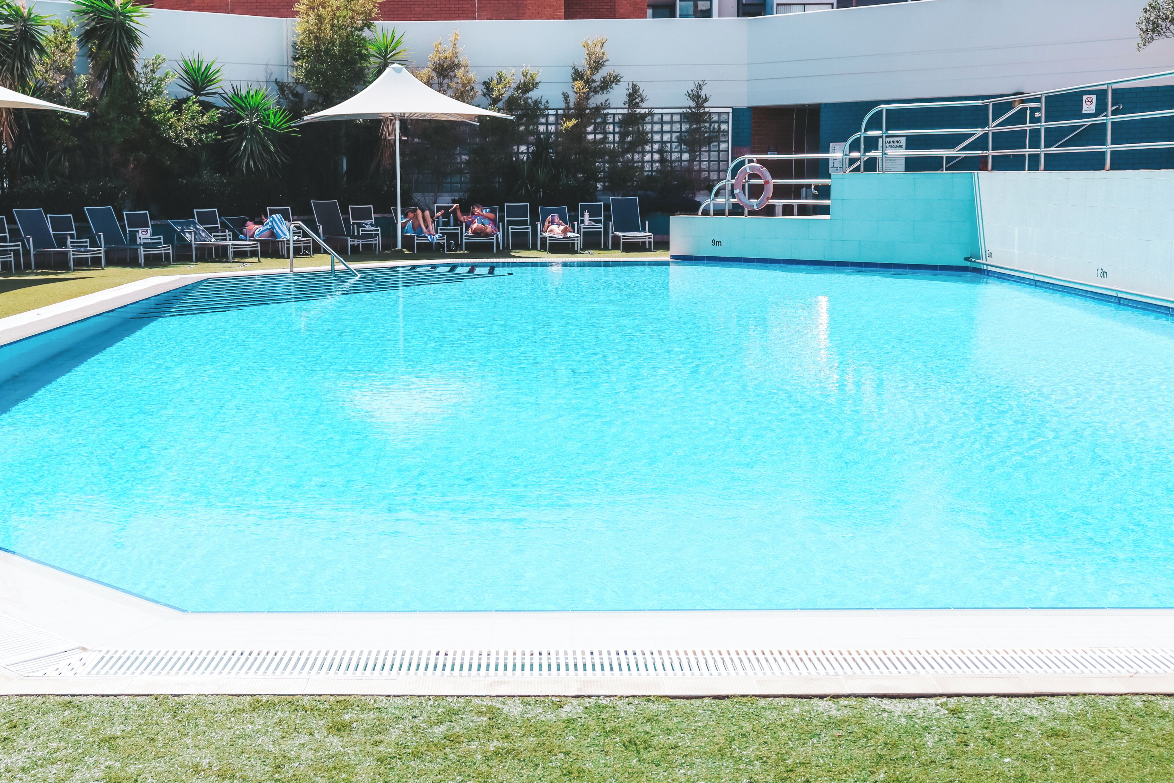 Una piscina con sillas de descanso, un puesto de salvavidas y un edificio al fondo.