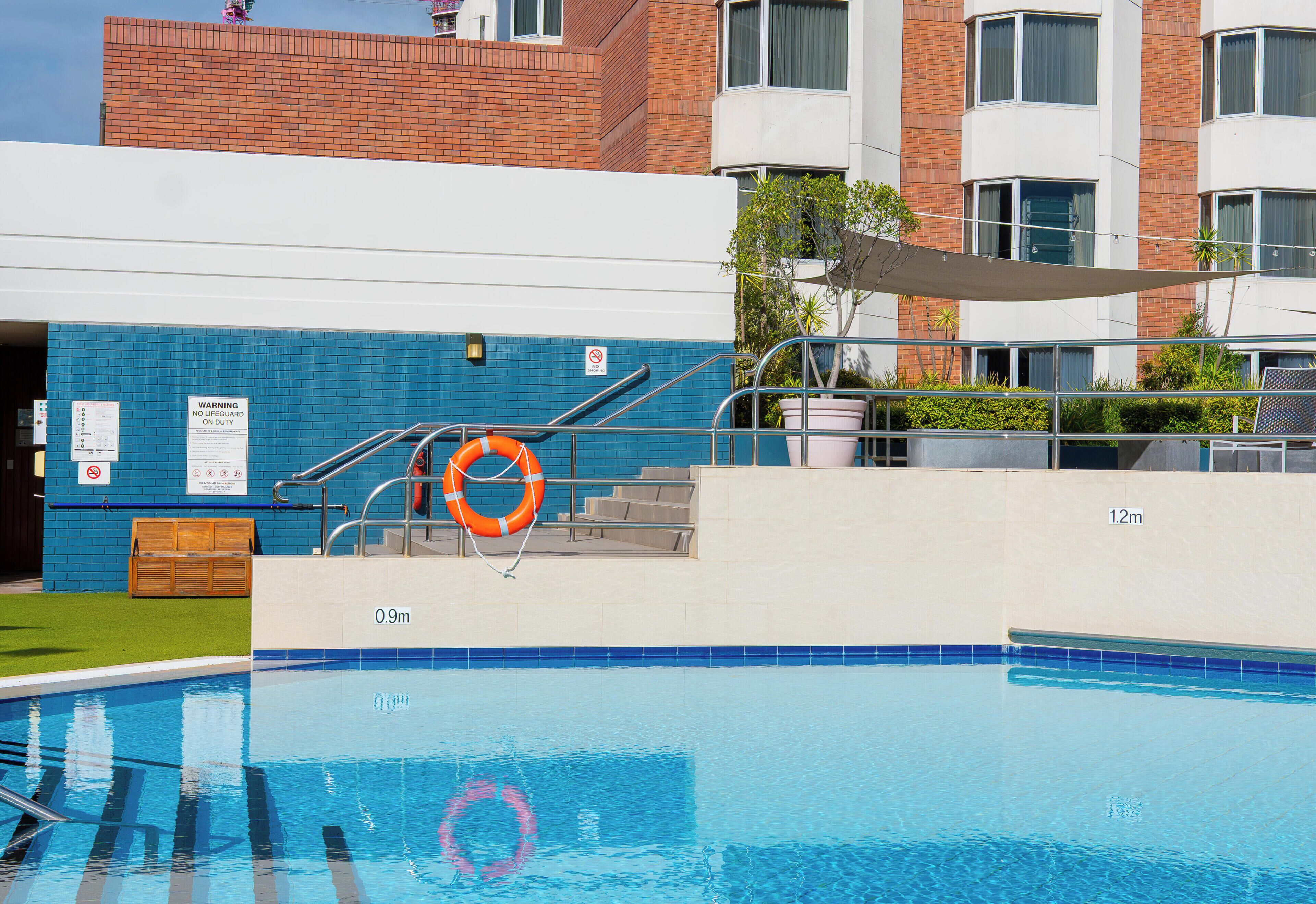 A swimming pool with steps leading into it, a lifebuoy, and a warning sign.