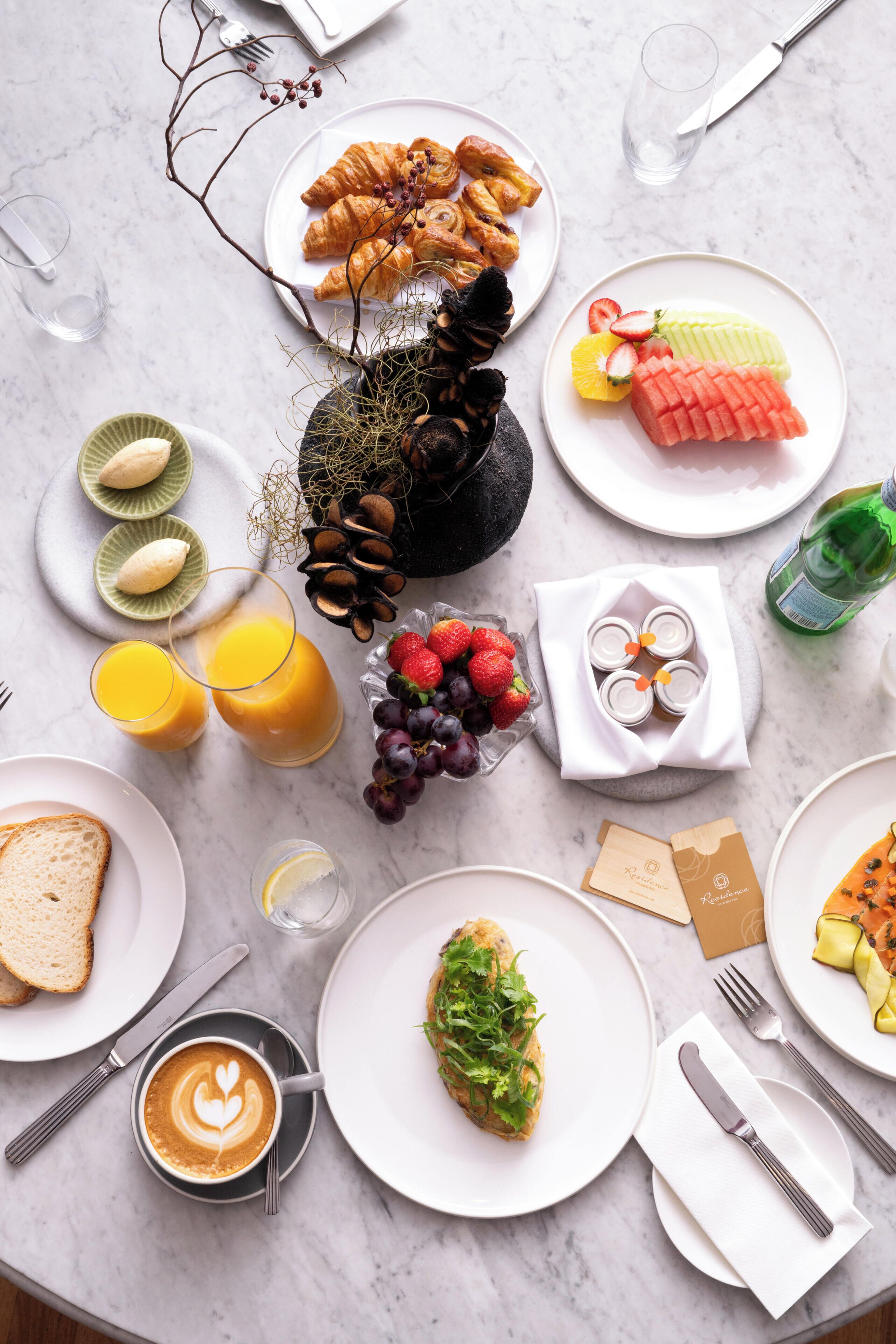 Desayuno con cruasanes, frutas, jugo y café sobre una mesa de mármol.